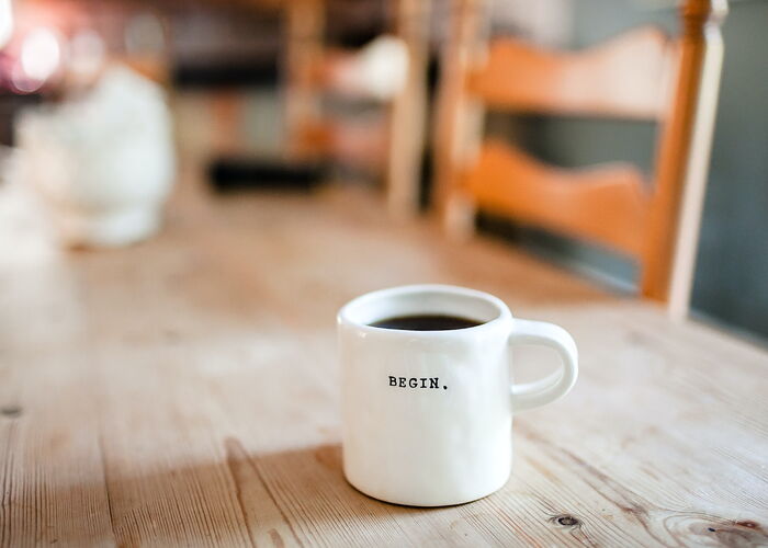 Photo : Une tasse de café remplie, blanche avec inscrit BEGIN.