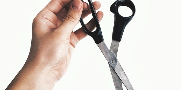 Photo : Une main tenant nonchalamment une paire de ciseau sur un fond blanc