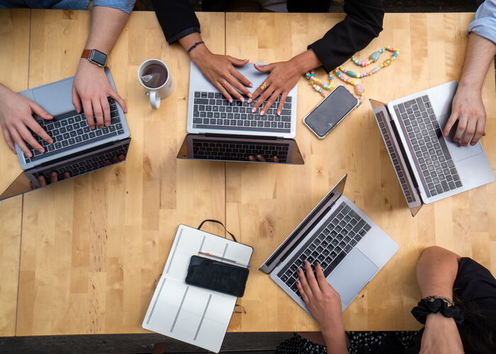 Photo : Vue du dessus d'une table de réunion avec 4 ordinateurs et 4 personnes travaillant ensemble