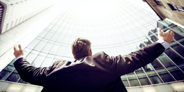 Photo : un décideur levant les bras ouverts vers un immeuble pour essayer de prendre en compte l'ensemble de son entreprise