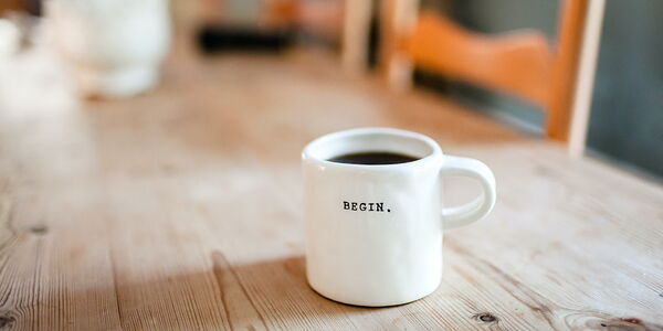 Photo : Une tasse de café remplie, blanche avec inscrit BEGIN.