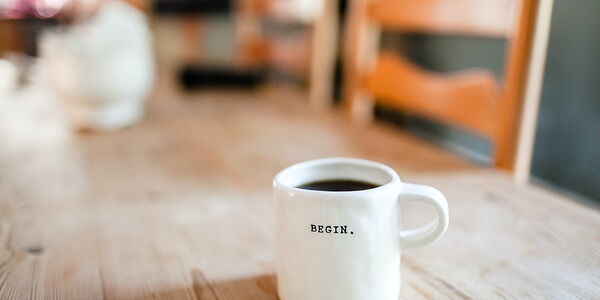 Photo : Une tasse de café remplie, blanche avec inscrit BEGIN.