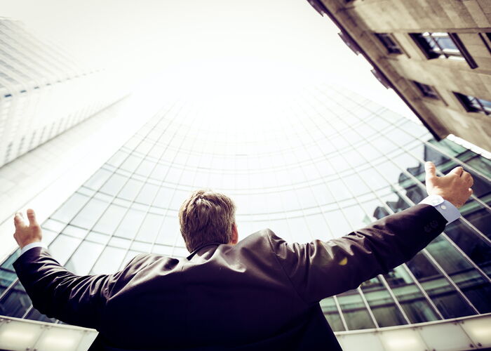 Photo : un décideur levant les bras ouverts vers un immeuble pour essayer de prendre en compte l'ensemble de son entreprise